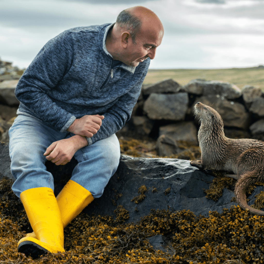 A scene from National Geographic's Billy and Molly, showing a man leaning towards an otter, to be shown at Wildscreen Festival 2024